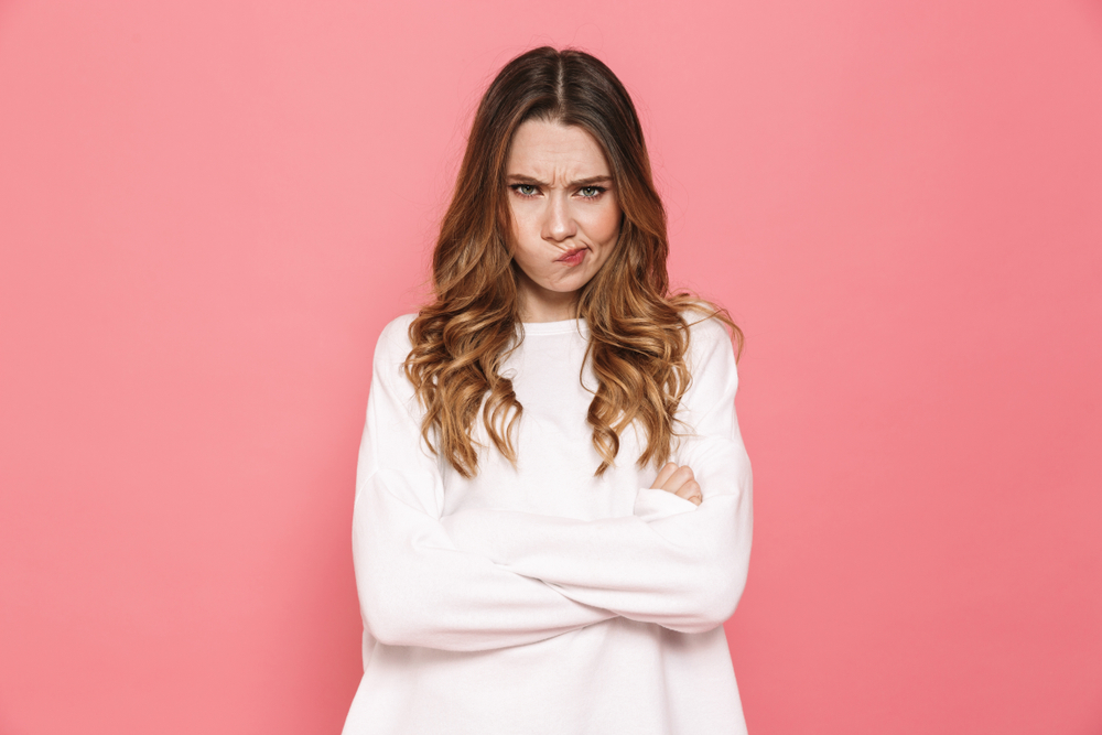 Portrait of an upset young casual girl standing with arms folded isolated over pink background