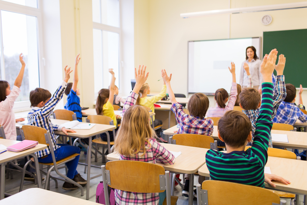 education, elementary school, learning and people concept - group of school kids with teacher sitting in classroom and raising hands