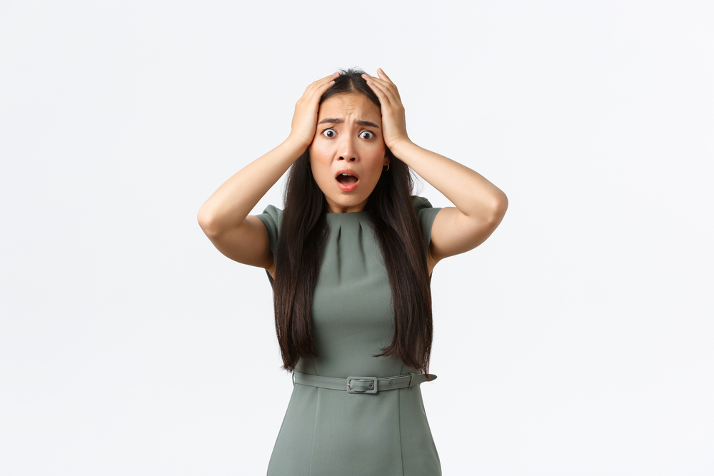 Small business owners, women entrepreneurs concept. Shocked asian woman in panic, grab head and looking startled with concerned alarmed face, being robbed, standing white background